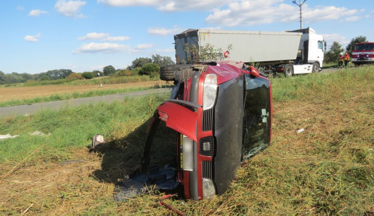 Řidič náklaďáku přehlédl pomalu jedoucí osobák a narazil do něj. Jeho řidička skončila v převráceném voze na poli